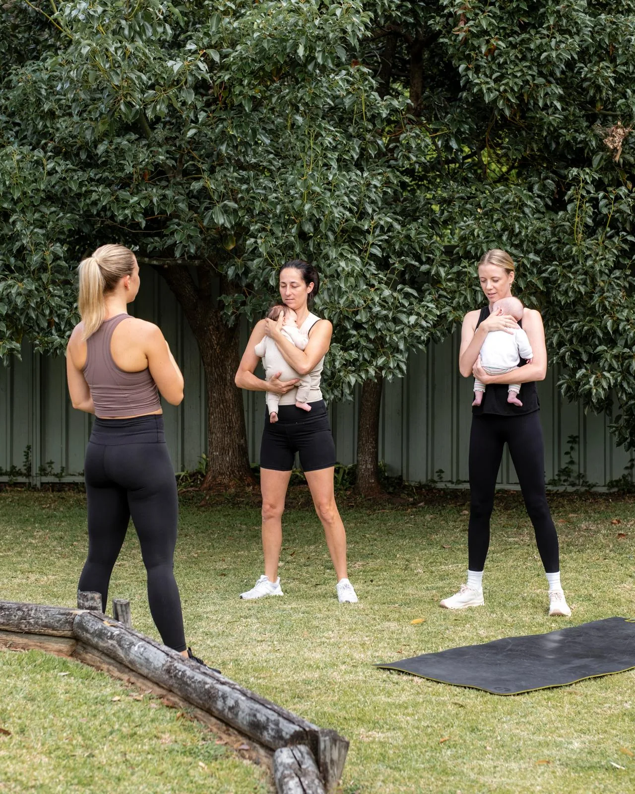 Tayla leading an outdoor session with two mothers standing on the grass holding their babies