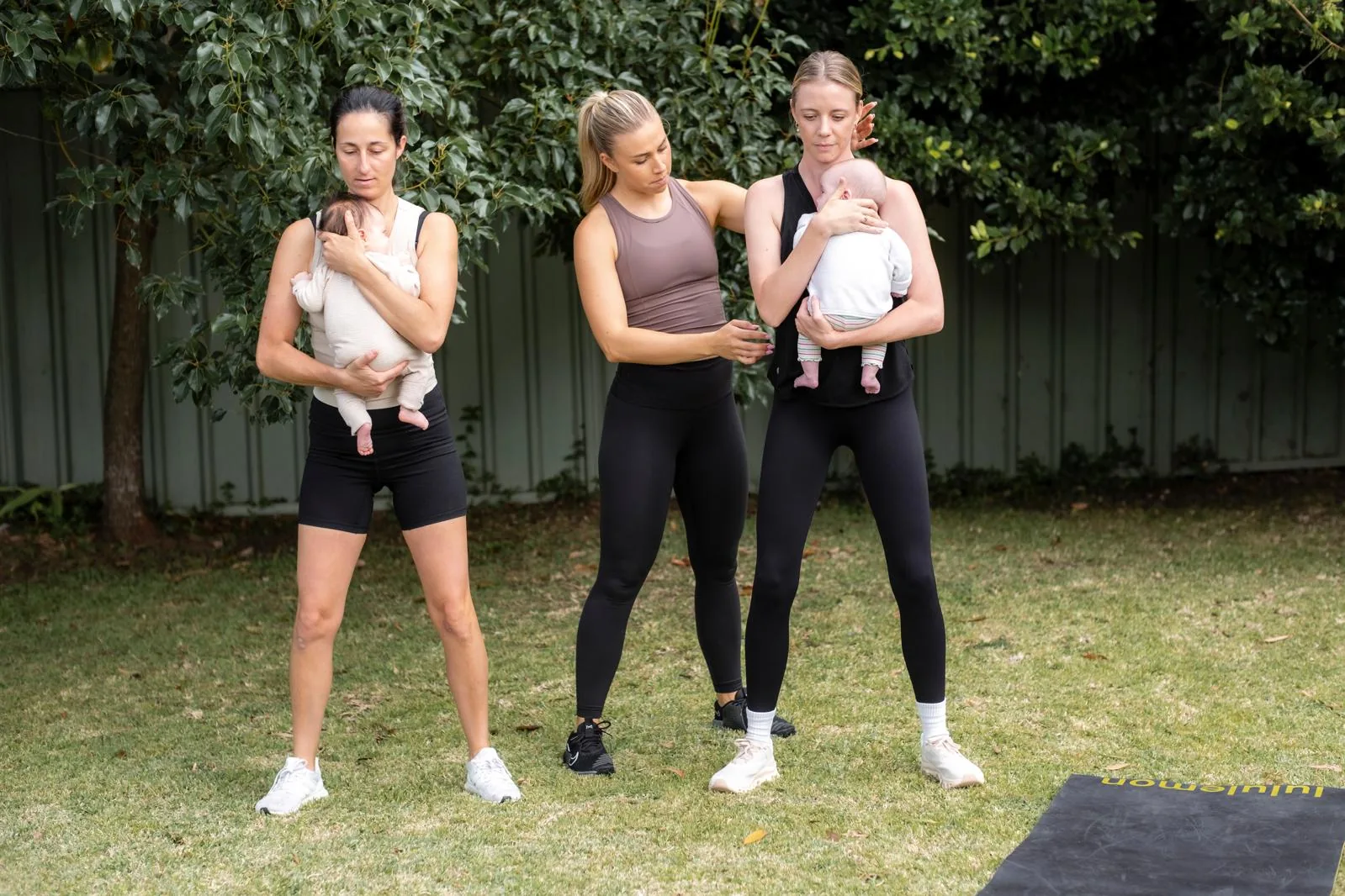 Tayla standing between two mothers holding their babies, guiding their position during an outdoor session